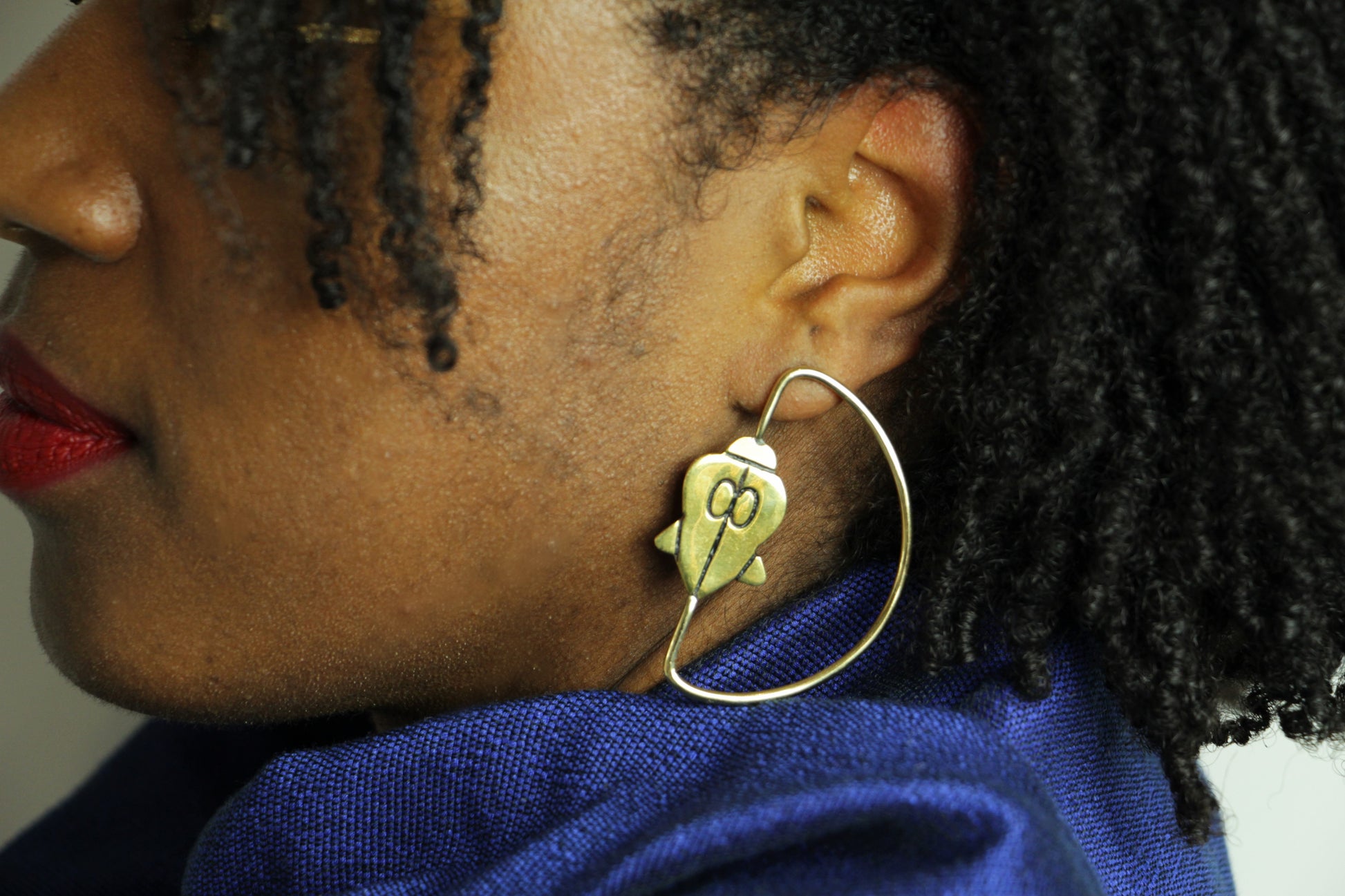 Les boucles d'oreilles Ifé, création de la boutique Jelani portées par une femme avec un drapé bleu